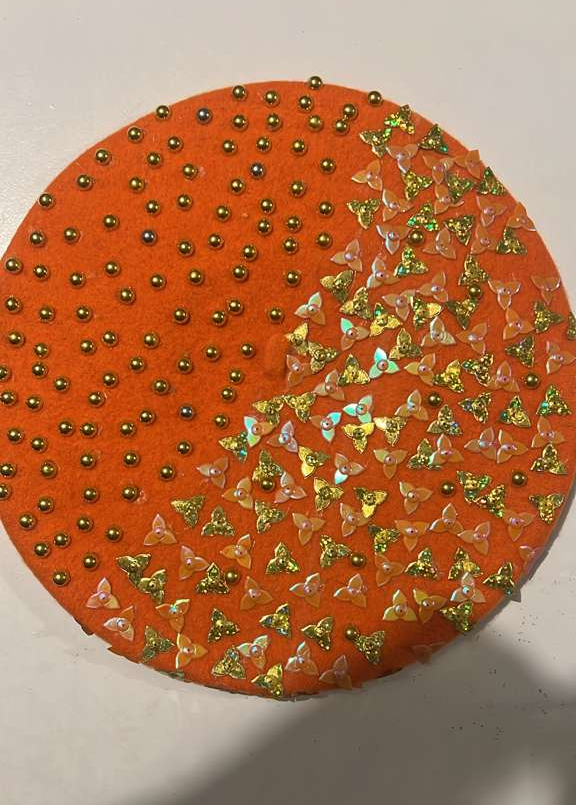 Orange felt beret covered in gold pearl studs on one half and gold glitter butterfly sequins on the other